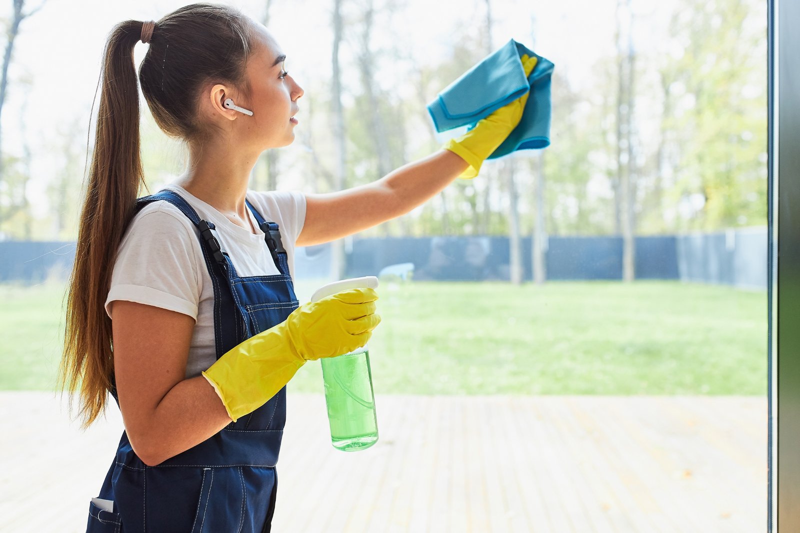 Een jonge schoonmaakster die een raam schoonmaakt met een doek en reinigingsspray.